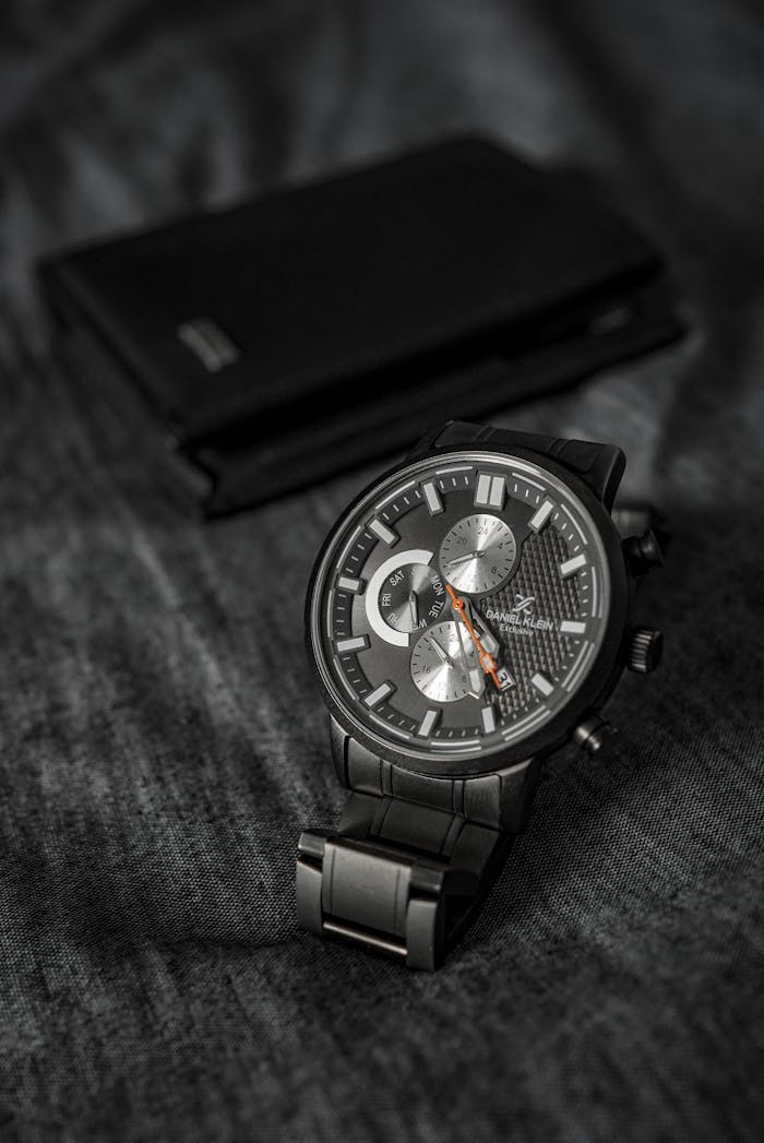menu-09 Close-up of a black wristwatch with metallic dial on a textured fabric background.