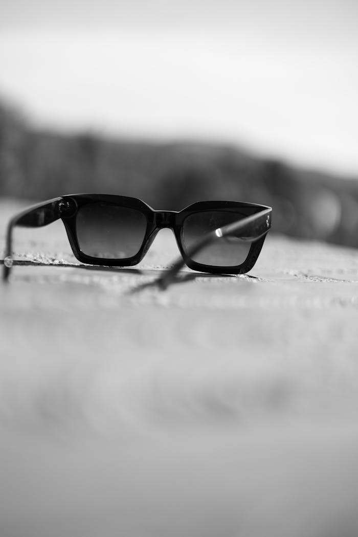 Black and white image of sunglasses lying on the ground with selective focus.