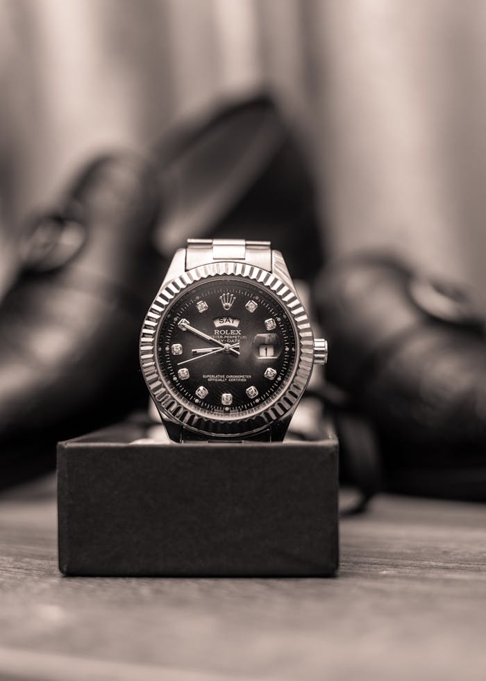 menu-15 Stylish wristwatch showcased with a blurred background of classic shoes, captured in black and white.
