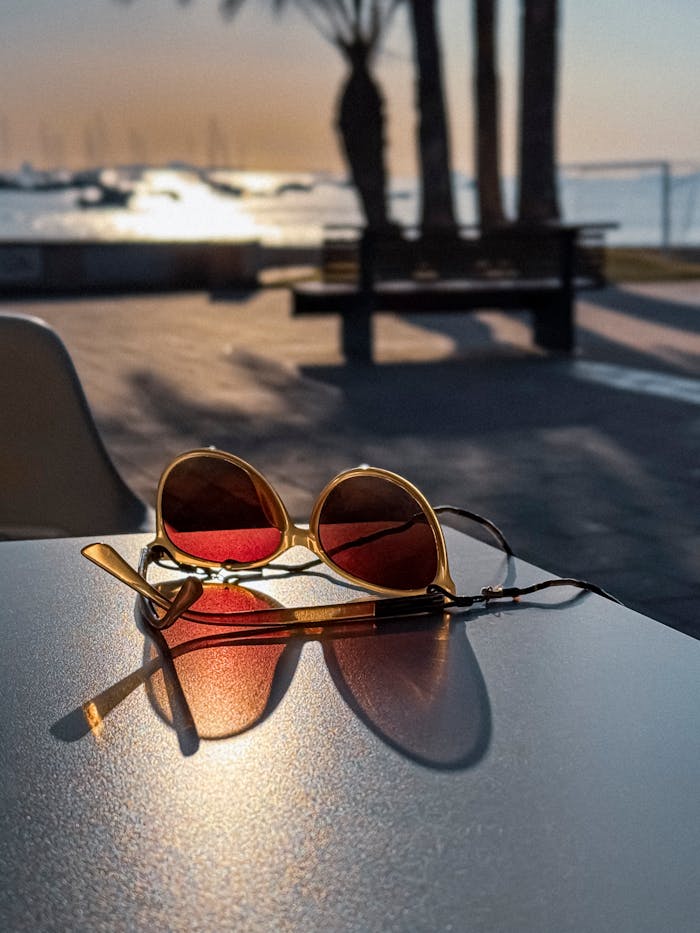 menu-17 Golden sunglasses rest on a table by the beach with a serene sunset and palm trees in the background.