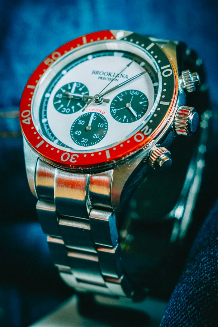 menu-14 Close-up of a stainless steel chronograph wristwatch with red bezel.