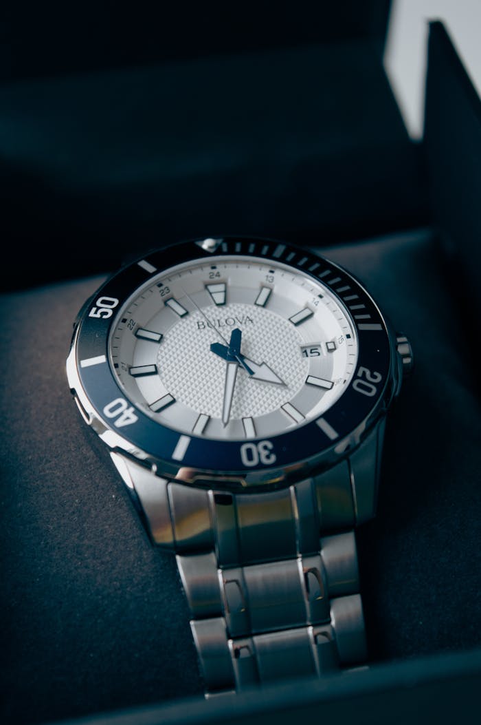 menu-16 Close-up of a luxury silver wristwatch with blue accents displayed in a box.
