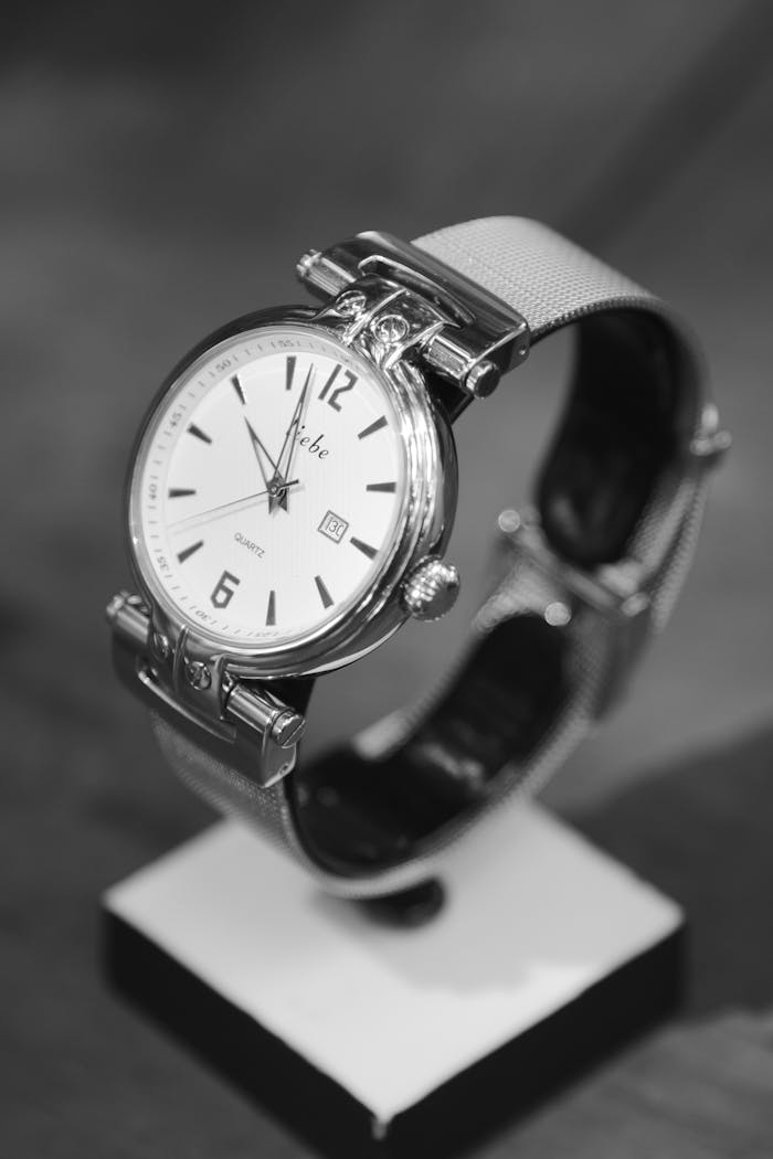 menu-06 Close-up of a classic silver wristwatch with leather strap on a stand.