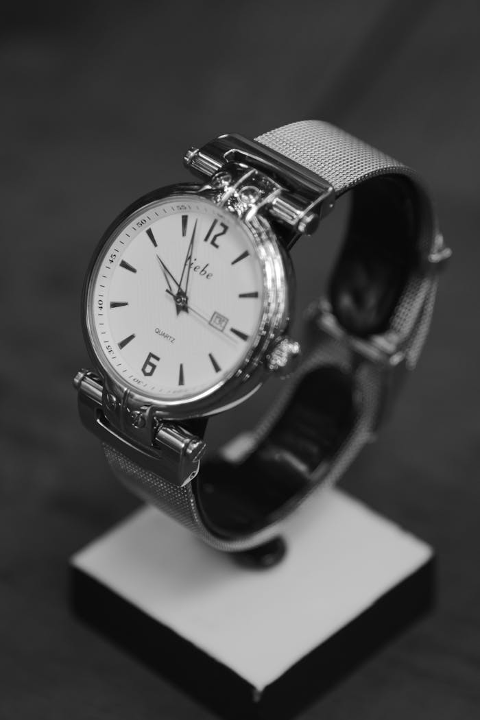 menu-12 Black and white image of an elegant silver wristwatch on a stand.
