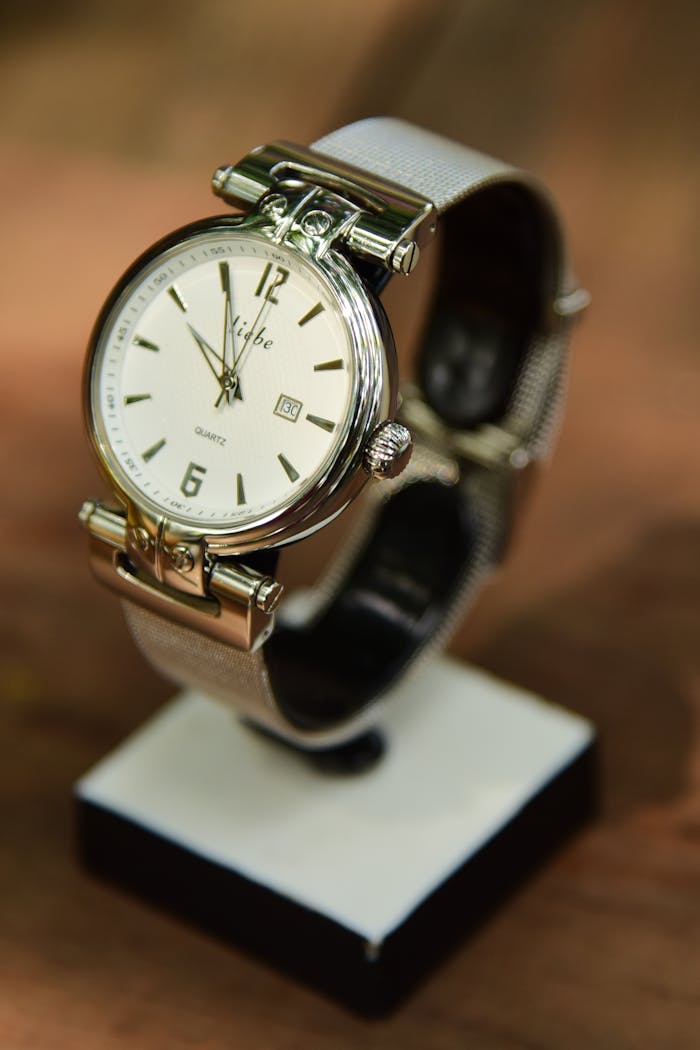 menu-10 Sophisticated silver wristwatch with an analog face elegantly displayed on a stand with a blurred background.