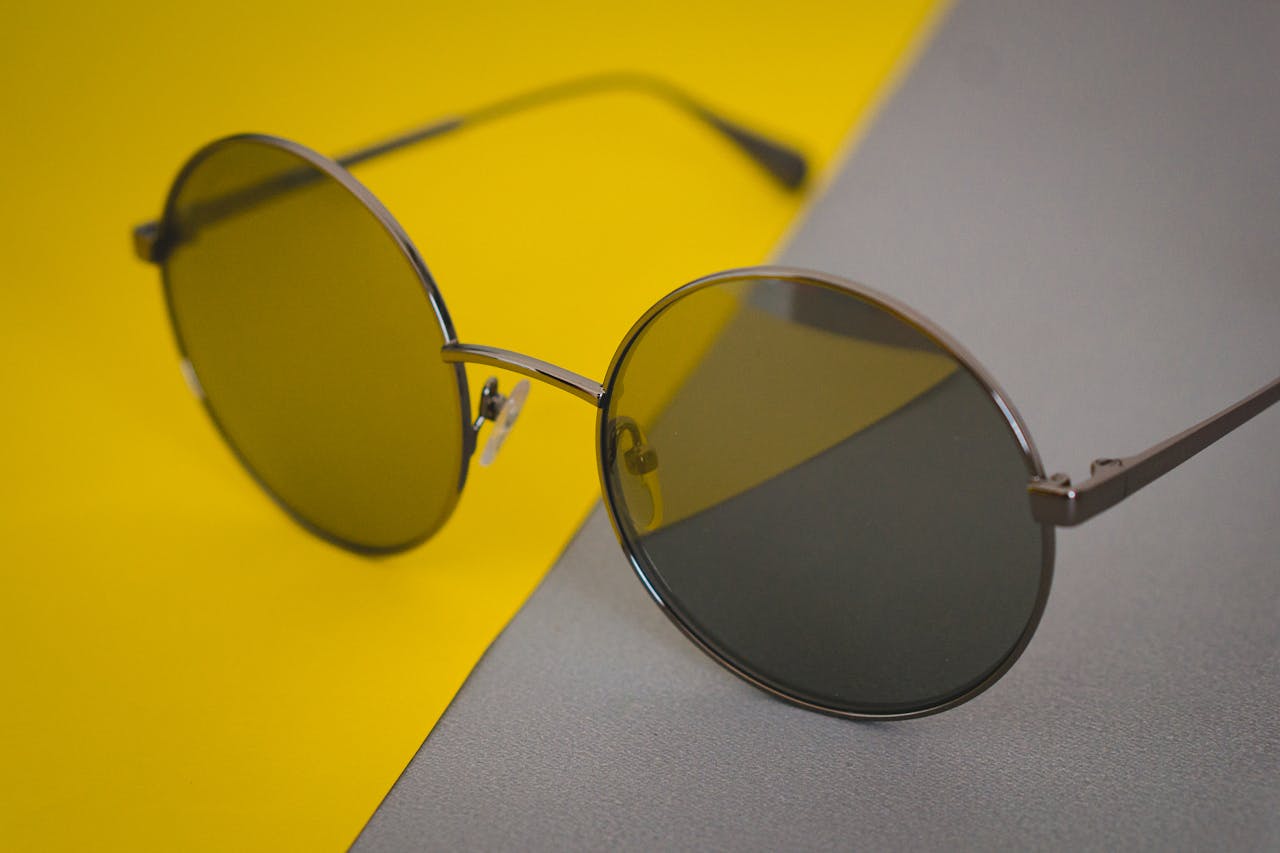 menu-18 Close-up of round sunglasses on a vibrant yellow and grey background. Perfect for fashion and accessory concepts.
