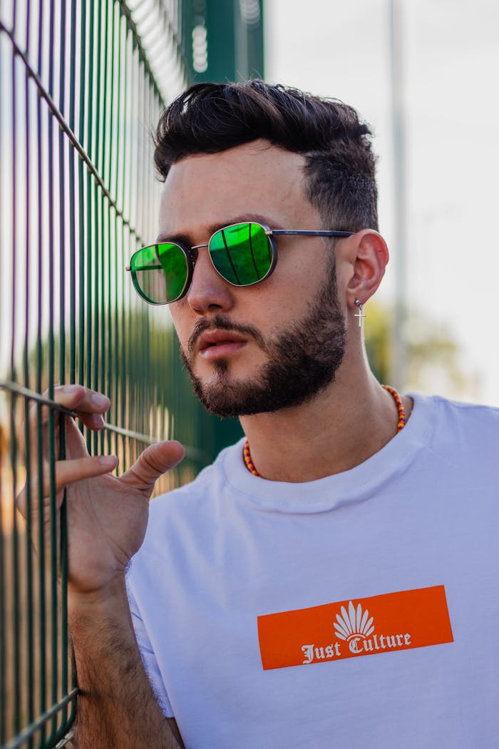 Mastering the First Impression: Your intriguing post title goes here Modern portrait of a bearded young man with green sunglasses by a metal fence.